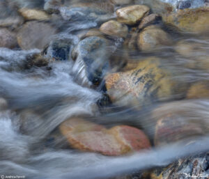 blurred water rushing across river stones in creek