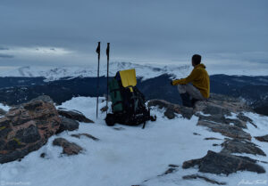 hiker sitting on snowy summit near mount evans april 2021