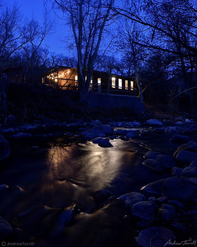 mountain cabin by creek with lights reflecting in water