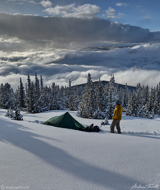 winter wild camping with tent and figure looking at view in snow with clearing storm clouds over rocky mountains in colorado