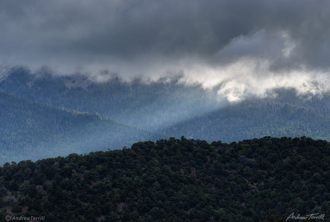 sunbeam shining over forest and mountains under storm cloud colorado