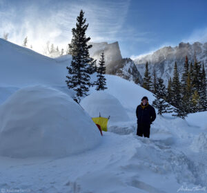 andrew terrill outside igloos with wind and spindrift swirling over ridge