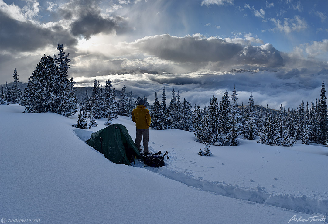 winter wild camping with tent and figure looking at view in snow with clearing storm clouds over rocky mountains in colorado