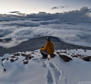 hiker sitting on mountain summit in winter in snow above the clouds