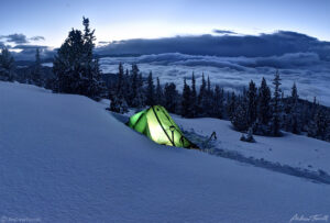 winter wild camping with glowing tent in snow with clearing storm clouds over rocky mountains in colorado